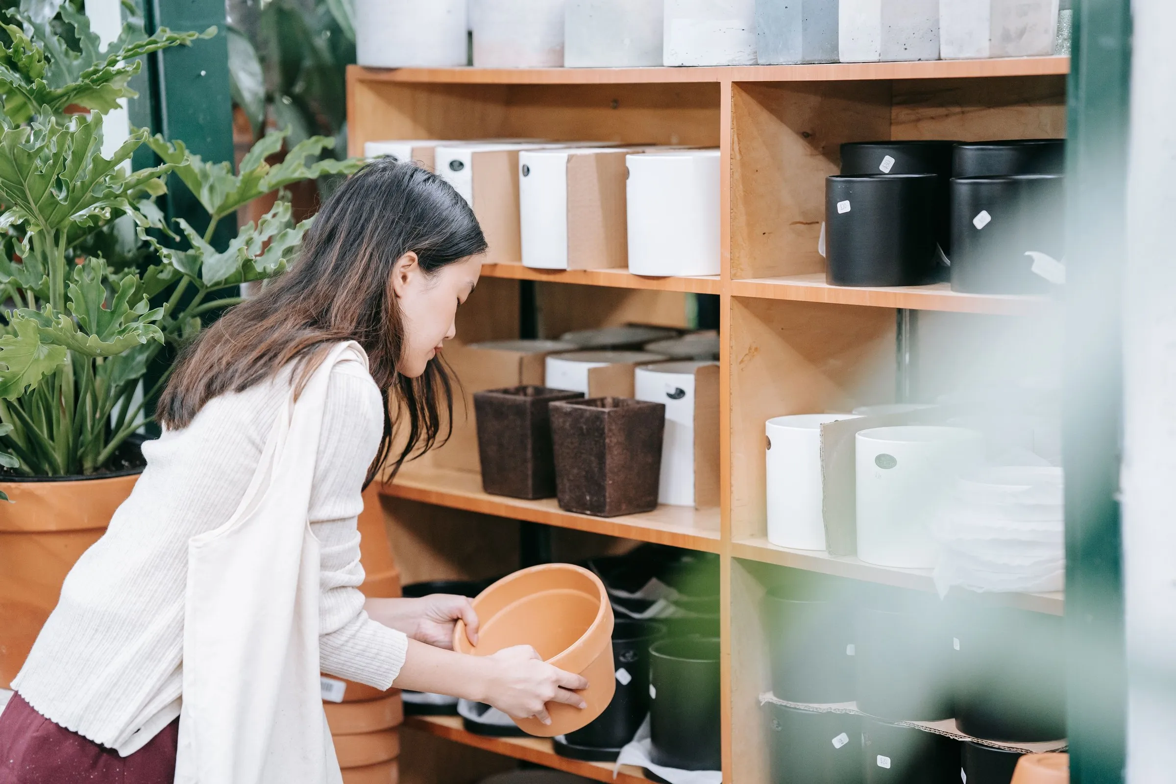 A woman browses planters on the shelves of a home goods store.