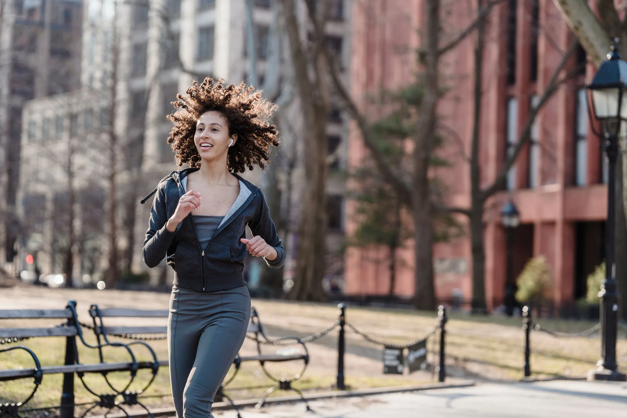 A smiling woman runs along a city park path on a sunny morning.