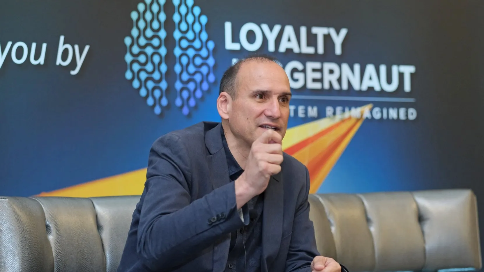 A speaker on stage at Loyalty Summit Americas in Chicago, in front of the Loyalty Juggernaut backdrop