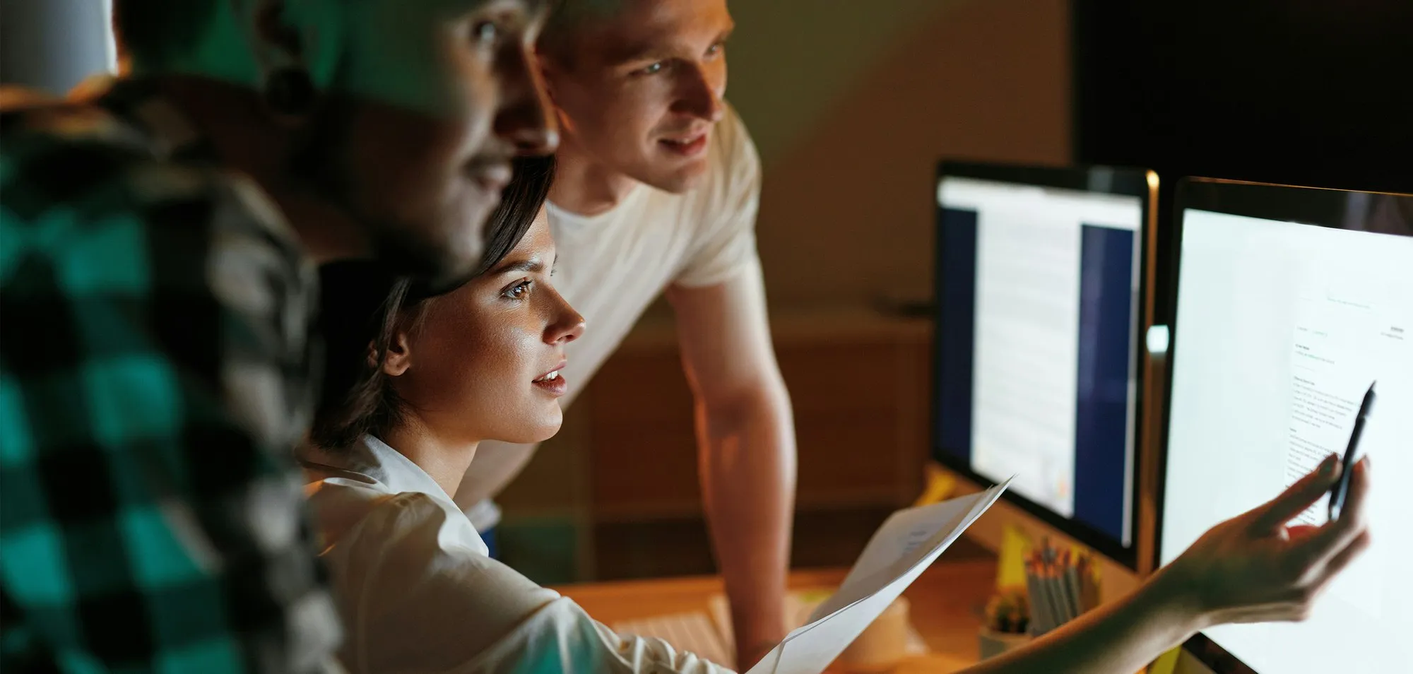 Three developers reviewing code together at a pair of monitors