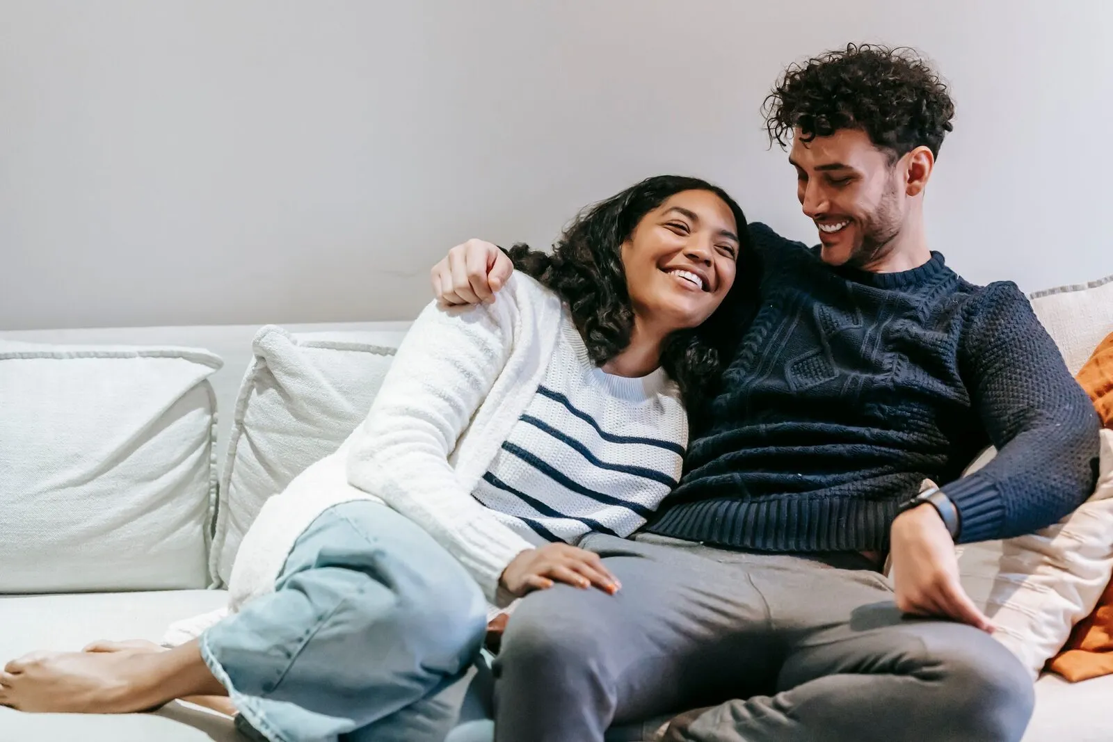A couple laughs together on a white sofa at home.