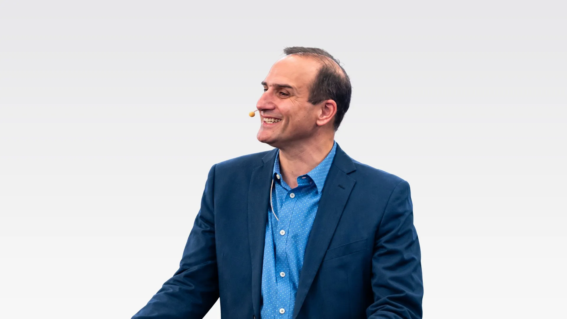 David Andreadakis, smiling, in a navy jacket and blue shirt, wearing a headset microphone