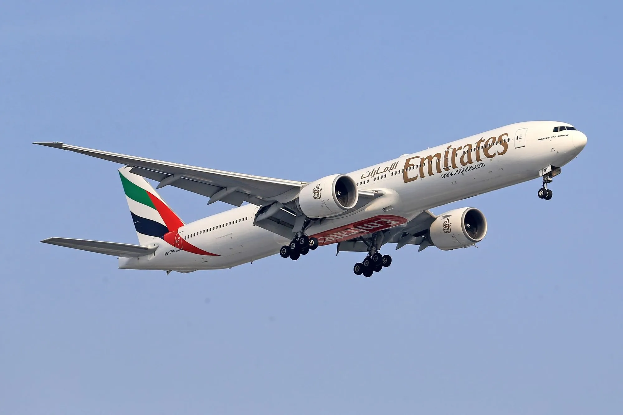 An Emirates Boeing 777 climbing out against a clear sky.