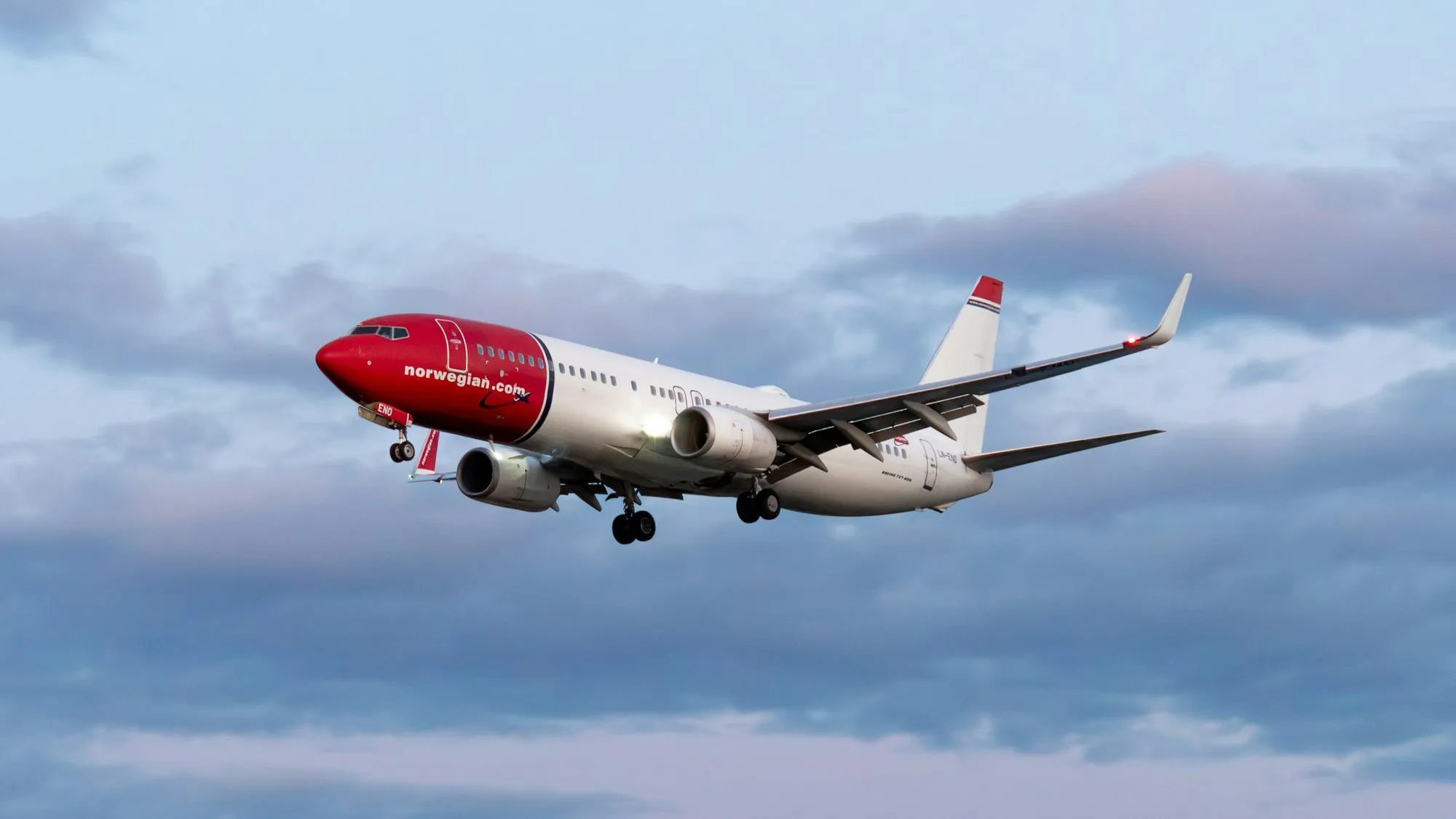 A Norwegian Boeing 737 on approach under an evening sky.