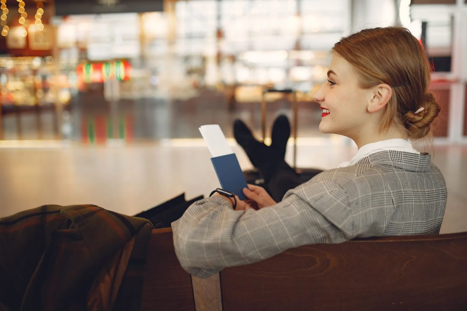 A smiling traveler waits in an airport terminal with her passport and boarding pass in hand.
